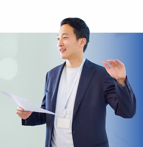 Man in business casual attire holding documents and gesturing while presenting, representing professional development and workplace training