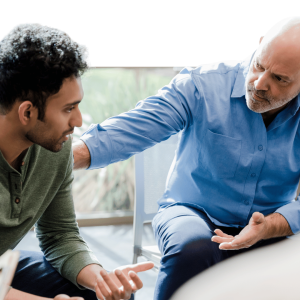 Older man in blue shirt placing supportive hand on younger man's shoulder during a mentoring or coaching conversation
