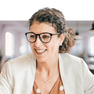 Woman wearing glasses and tan blazer smiling in modern office setting