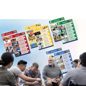 Group of adults discussing colorful program posters displayed outdoors, including DISC personality and workplace wellness training materials