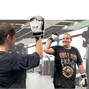 Woman in boxing gloves high-fives an instructor while smiling during a group fitness class with participants watching